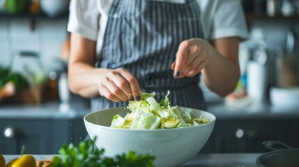 A young woman in a gray apron sipes a salad of Chinese cabbage - obrazy, fototapety, plakaty