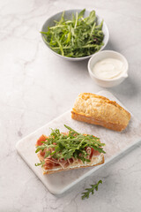Ciabatta Italian sub sandwich with prosciutto ham, arugula on marble light grey background. Italian cuisine concept