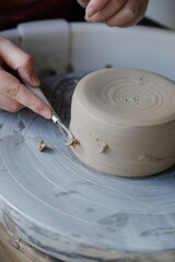 Vertical: Close up of a person trimming ceramics on a pottery wheel.