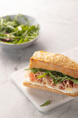 Ciabatta Italian sub sandwich with prosciutto ham, arugula on marble light grey background. Italian cuisine concept. Vertical