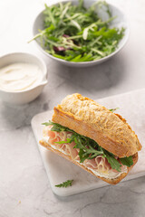 Ciabatta Italian sub sandwich with prosciutto ham, arugula on marble light grey background. Italian cuisine concept. Vertical