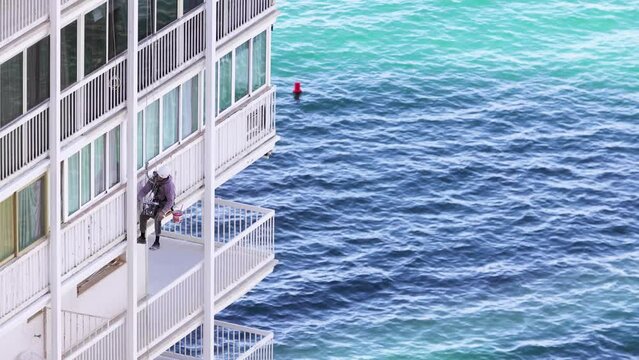 A man painting the side of a hotel building by the ocean in the town of Benidorm in Spain