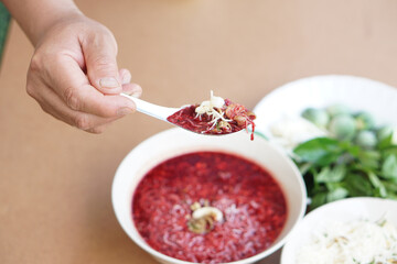 Hand hold spoon of red fresh blood mixed with minced pork ,Thai herbs ingredients. Spicy bloody...