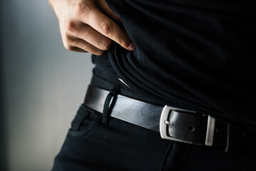 the waist of a man dressed in a black T-shirt and trousers and accented by a black leather belt