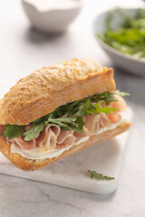 Ciabatta Italian sub sandwich with prosciutto ham, arugula on marble light grey background. Italian cuisine concept. Vertical