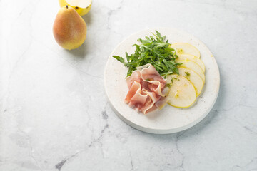 Summer pear salad with prosciutto, arugula on light great marble background. Healthy diet concept....