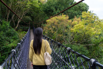 Woman walk along the suspension bridge in the forest - 762414572