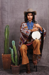 Portrait, cowgirl or woman with instrument for music in studio and cool fashion or clothing on grey...