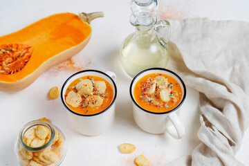 Roasted butternut squash soup with cream and pumpkin seeds on two white mugs.