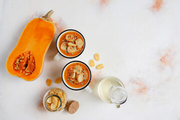 Roasted butternut squash soup with cream and pumpkin seeds on two white mugs.