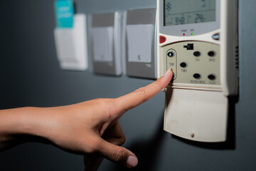 Finger pressing an air conditioner remote control and light switch on white concrete wall.