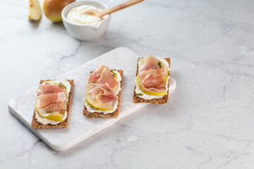 Ideal snack wholewheat crispbread with ricotta cheese, prosciutto, sliced pear and thyme on light...