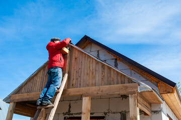 A worker builds a roof in a house while standing on a wooden ladder. Blue sky - 762424378