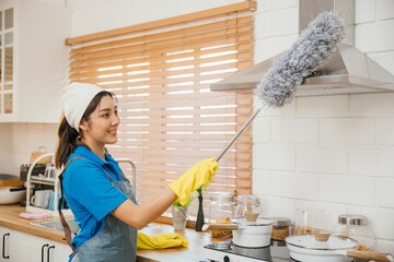 Maid in workwear and gloves cleans home dusts kitchen ventilation. Emphasizing modern housework...
