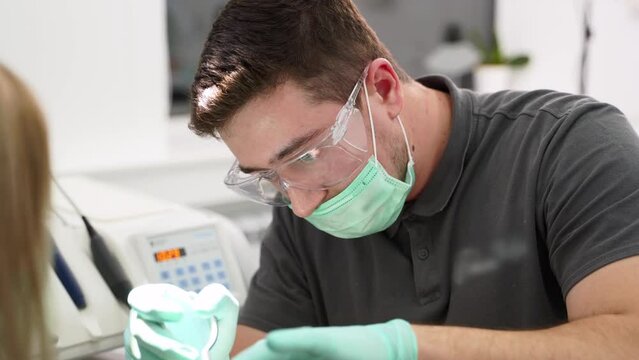 Professional dentist in protective glasses, mask pulling a tooth out. Concentrated dental surgeon works with dental nippers. Caucasian male doctor treats patient in the modern dental clinic. Close-up.