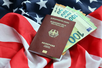 Red German passport of European Union and money on United States national flag background close up....