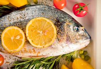 Sea bream fish dorado with tomato cherries and lemon slices on white plate. Top view.