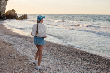 A middle-aged woman with a braid, in a cap and shorts, on the seashore. Travel and tourism.