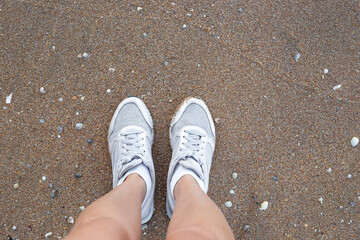 Female legs in white sneakers on the sandy beach. Travel and tourism.