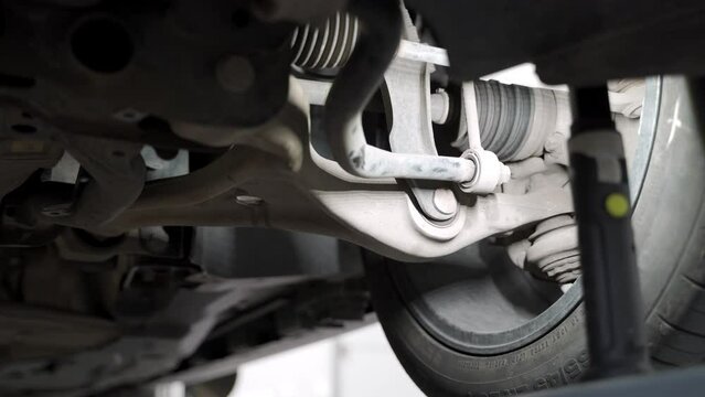 Auto mechanic adjusts car wheel alignment in service garage. Technician uses tools on vehicle suspension for precise tire adjust. Workshop work, maintenance process shown in detail.