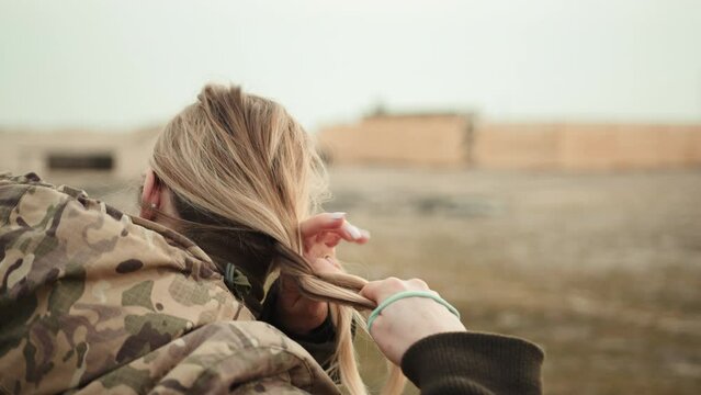 In a moment of calm during the turmoil of war, a female soldier methodically braids her hair, exhibiting serenity and poise in the face of adversity. Camera 8K RAW. 
