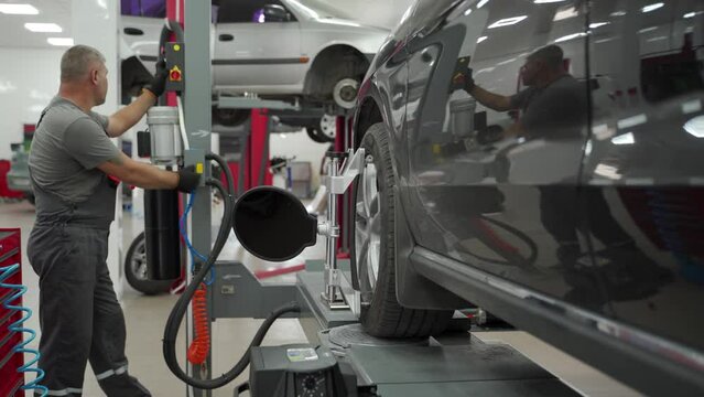 Auto mechanic aligns car wheel with high precision equipment at vehicle service center. Expert conducts alignment check on modern automotive, ensures optimal performance for safety.