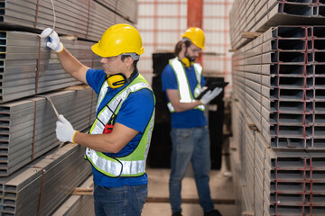 Caucasian engineers with yellow hardhat inspect steel bars with tablet in a factory