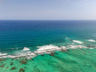 Aerial drone view of turquoise Caribbean Sea with small waves and coral reef on a cloudless sunny day in Tulum