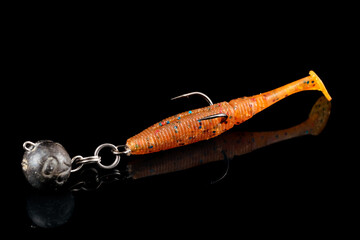 Orange fishing lure, plastic shad fish, with double hook and lead sinker, isolated on black