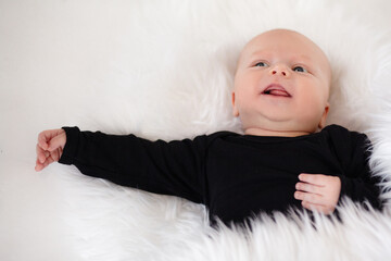 Ilittle baby dressed in a faithful bodysuit is lying on a white plush blunket