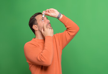 Young man dropping eye lubricant to treat dry eye or allergy while standing on green background
