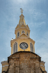 Cartagena, Colombia - July 25, 2023: Frontal, Top of Torre del Reloj and gate in remaining part of ramparts into old town center, square on SE side under light blue cloudscape