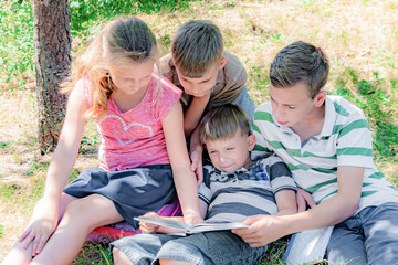 Friendly children in the park read a book sitting on the grass.