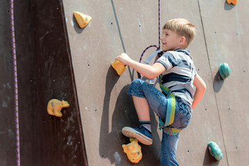 A boy in climbing equipment conquers the top of an artificial tower for climbers in a sports...