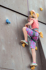 A girl creeps up on an artificial rock-climbing tower with insurance in an extreme sports park.