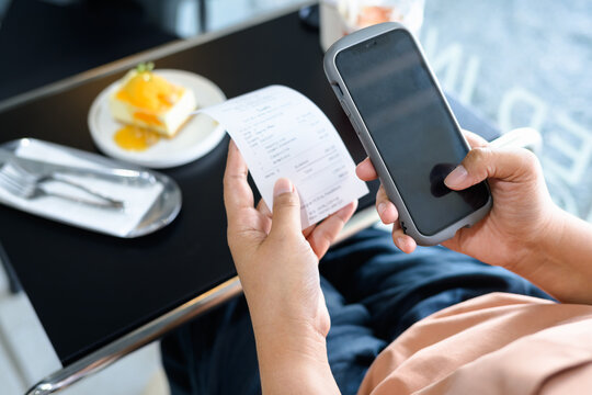 Closeup woman using smart phone with food bill in the coffee shop, calculating the price, scan payment