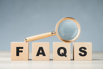 FAQS abbreviation (Frequently Asked Questions) in a row of wooden cubes, with magnifying glass