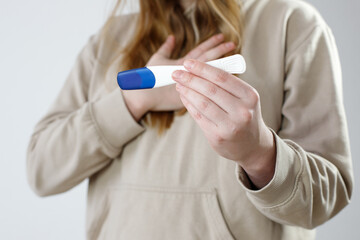Close-up shot of a woman looking at a pregnancy test. She checks the pregnancy exam. Details of a girl's hand holding a pregnancy test. Shallow depth of field with focus on pregnancy test. - obrazy, fototapety, plakaty
