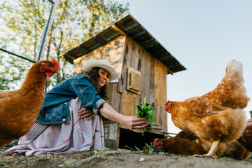 Happy middle aged woman on a private farm feeding chickens. Joyful farmer woman caring for her bird...