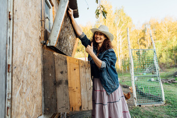 Smiling female farmer takes out a freshly laid egg in the chicken coop. A cheerful curly woman demonstrates an egg in her country house.