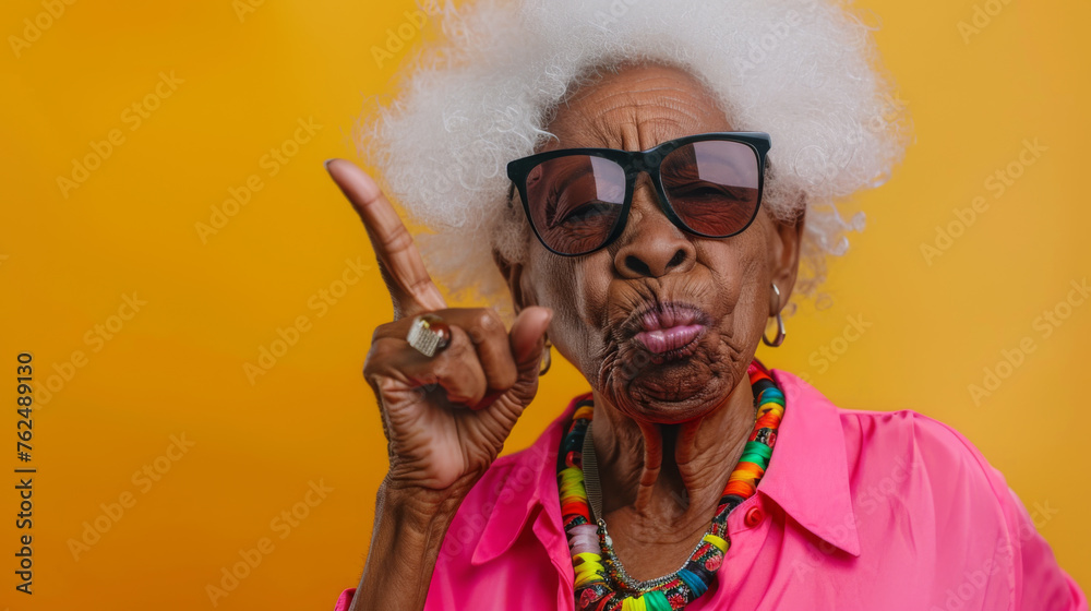 Wall mural a spirited elderly woman with sunglasses pointing with panache against an orange backdrop.