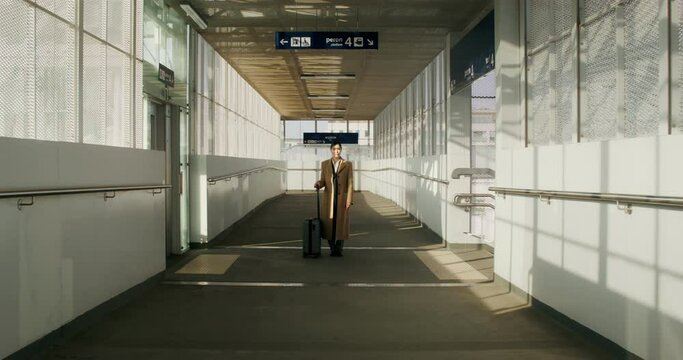 A woman in a coat with luggage in her hand stands at the railway station. She looks at the camera with a serious look