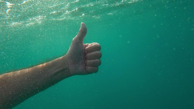 Man gesturing thumbs up underwater in deep sea water as sign of endorsement and approval