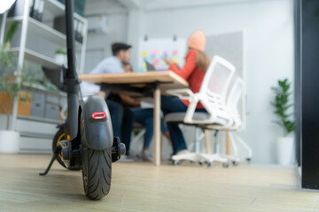 Selective focus of electric scooter in modern office with group meeting blurred background
