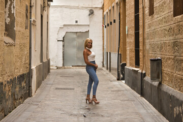 Fototapeta na wymiar Mature, beautiful, blonde woman in white top and jeans, posing in funny attitude on a lonely city street. Concept beauty, fashion, trend, travel, maturity.