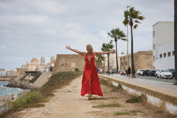 Mature woman, beautiful, blonde, with a red dress, walking with open arms, grateful, full of happiness, while the wind blows her hair and her dress. Concept beauty, fashion, trend, travel, maturity.