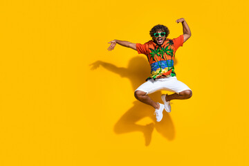 Fototapeta na wymiar Full length photo of optimistic guy wear hawaii shirt in glasses jumping directing at logo empty space isolated on yellow color background