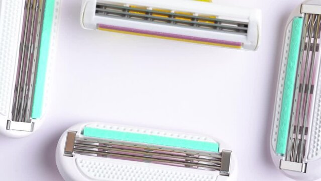 Frame of pink and yellow disposable razors on white table, copy space. Macro shoot of the razor blade, rotation.