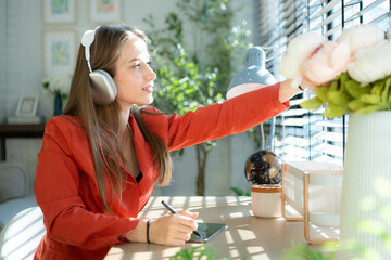 Young woman with headphones listening to music while sitting at table in room