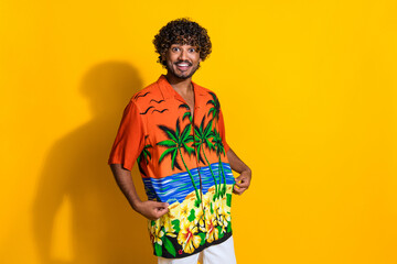 Photo of overjoyed satisfied impressed man with curly hairstyle fingers hold print shirt isolated on vibrant yellow color background